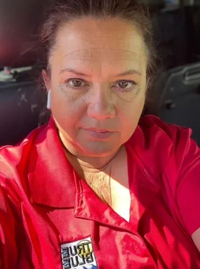 Selfie of a person in a red shirt, lit by sunlight inside a car.