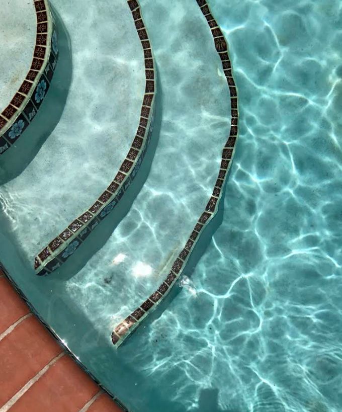 Curved pool steps with dark tile edges in clear turquoise water, beside a terracotta deck.