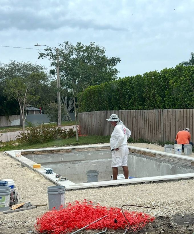 Workers constructing a backyard swimming pool with a white concrete frame and gravel surround