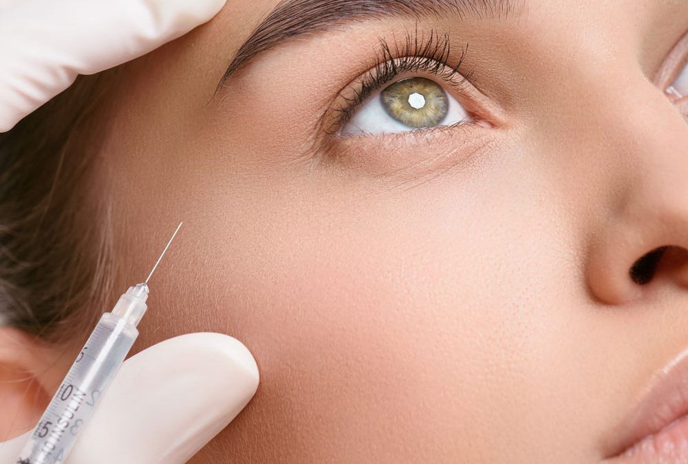 Close-up of a face while a gloved hand holds a syringe near the cheek