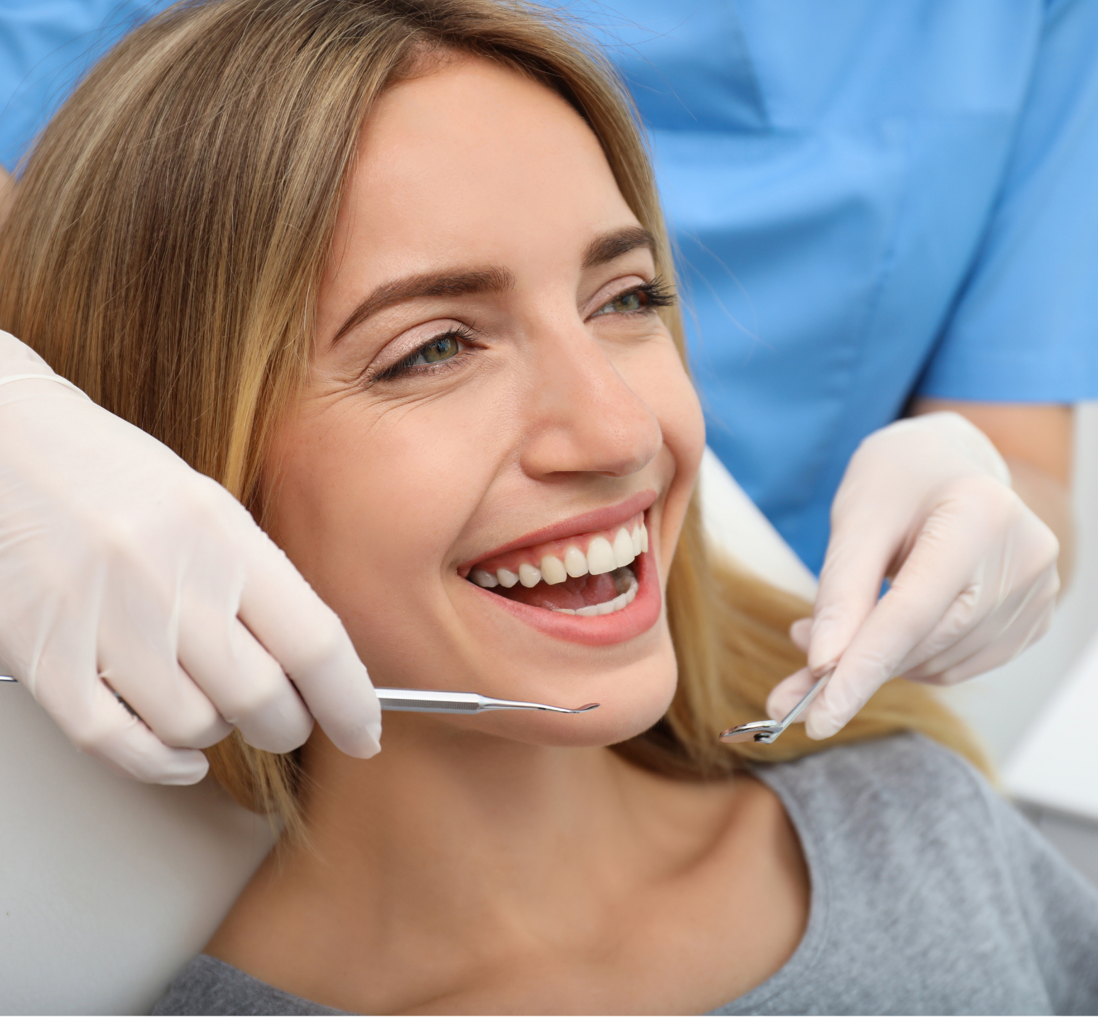 Smiling patient at a dental exam with gloved hands holding mirror and tool