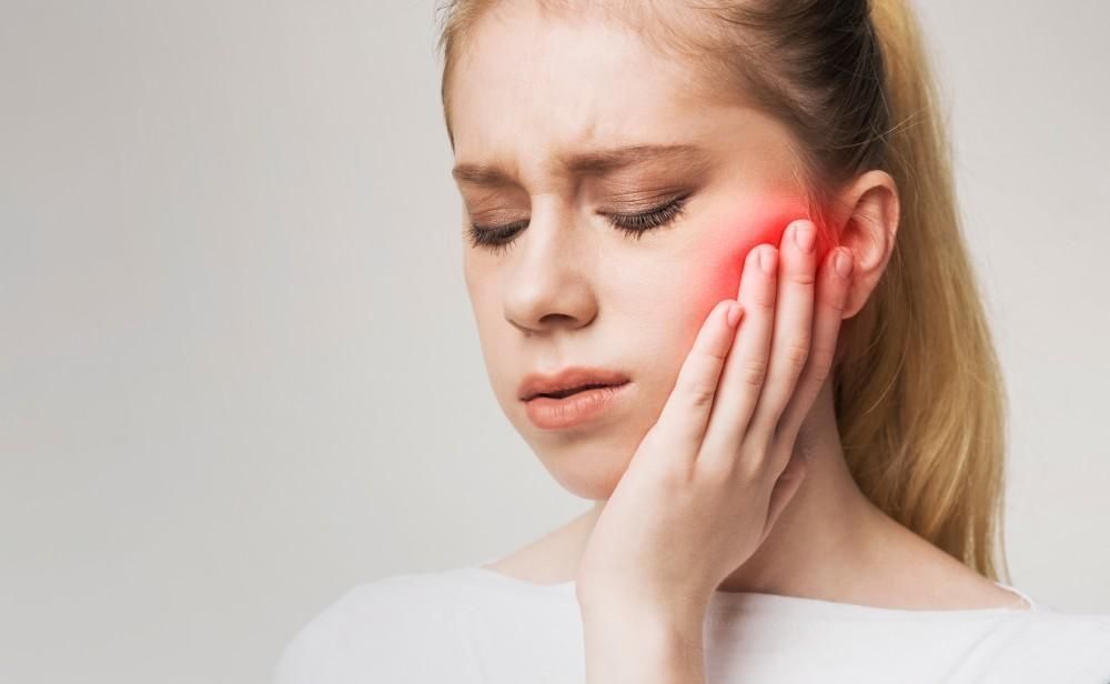 Person holding cheek with a red glow, suggesting tooth or jaw pain