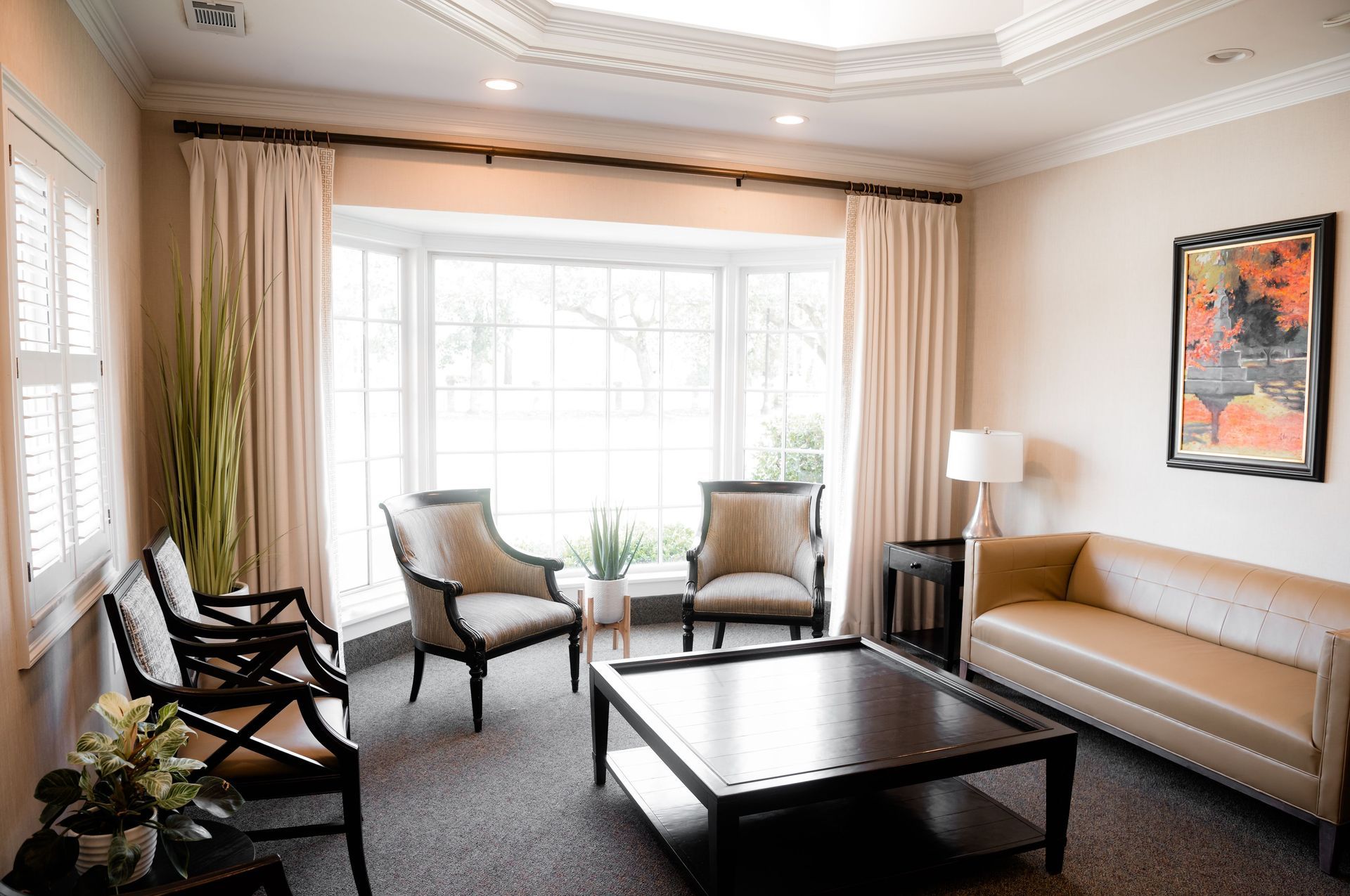 Bright living room with large windows, beige sofa, chairs, coffee table, and framed wall art