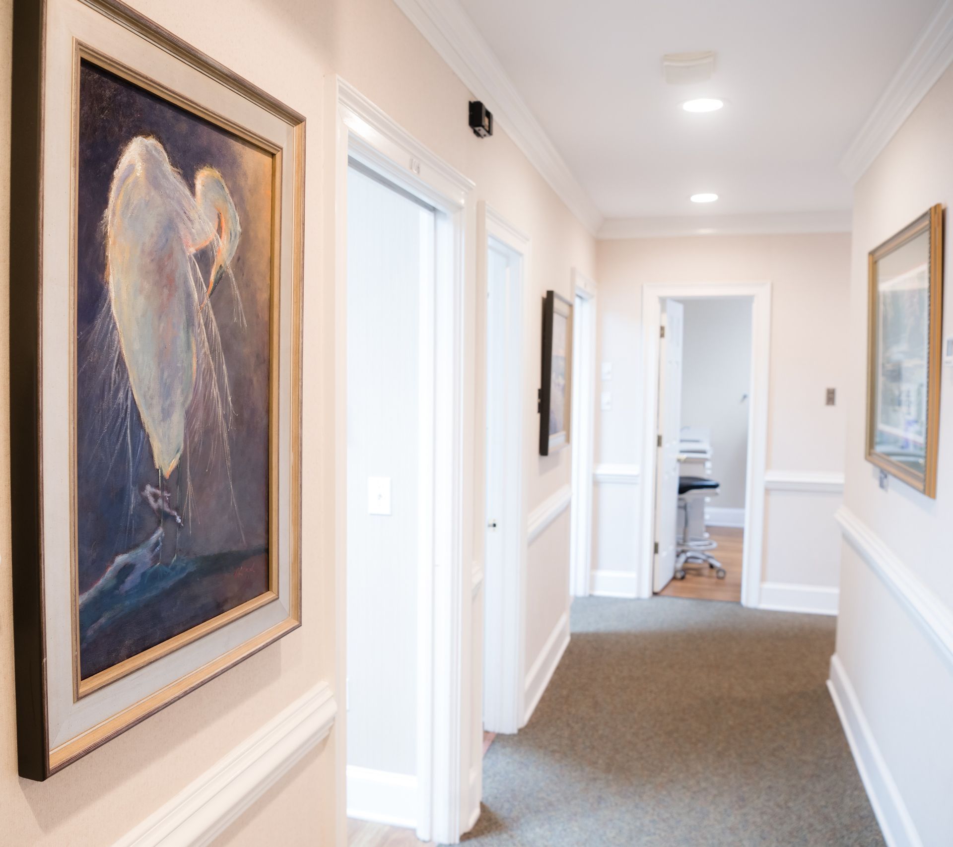 Bright hallway with framed art, white walls, and carpet leading to a doorway.