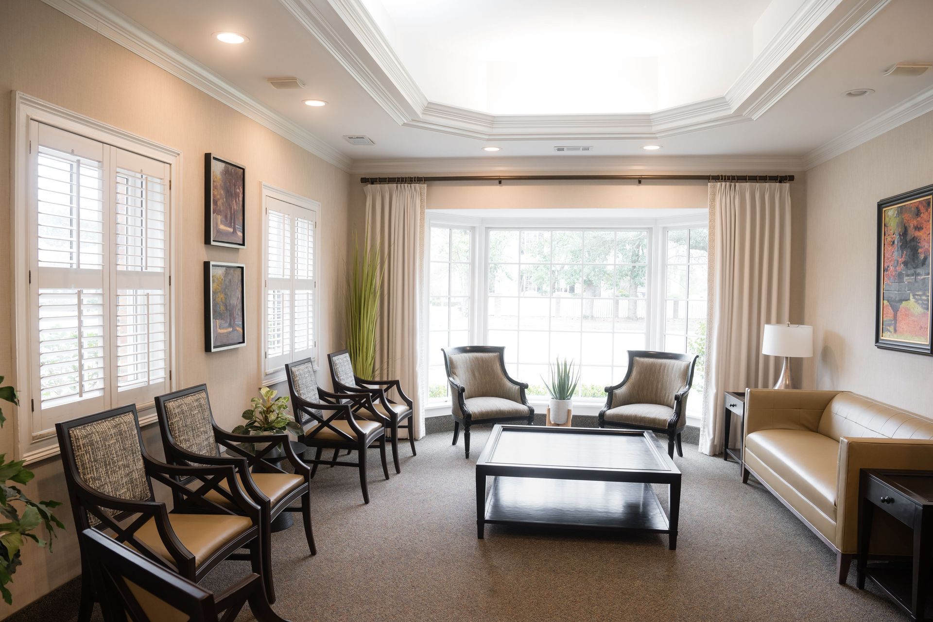 Elegant living room with chairs, sofa, and coffee table facing large windows and curtains