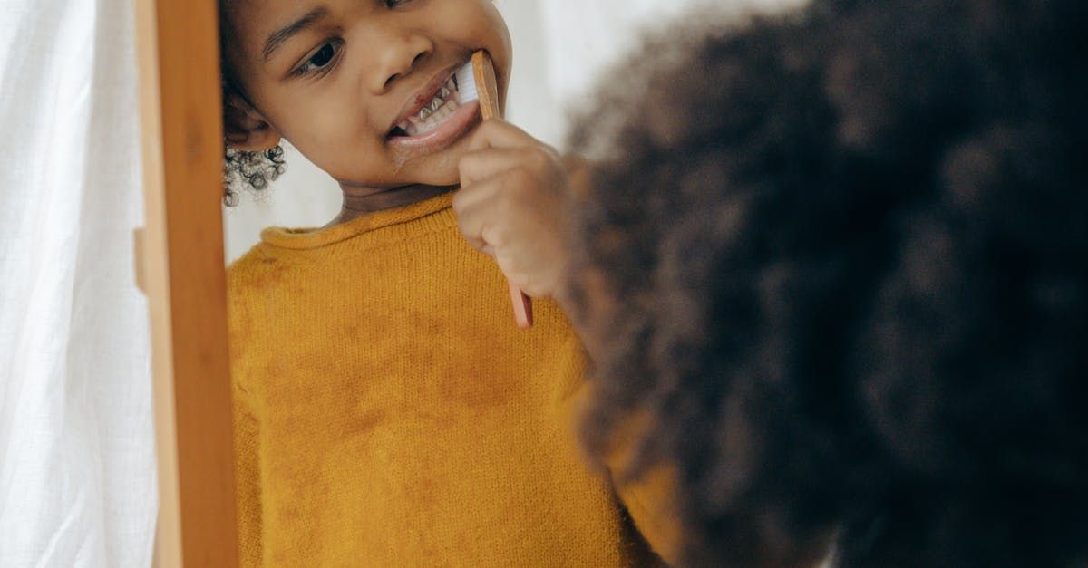 Person smiling in a mirror while brushing their teeth, wearing a mustard yellow sweater.