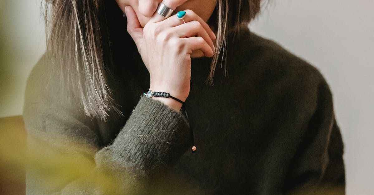 Close-up of a person in a dark sweater resting a hand near their face, wearing a turquoise ring and bracelet.
