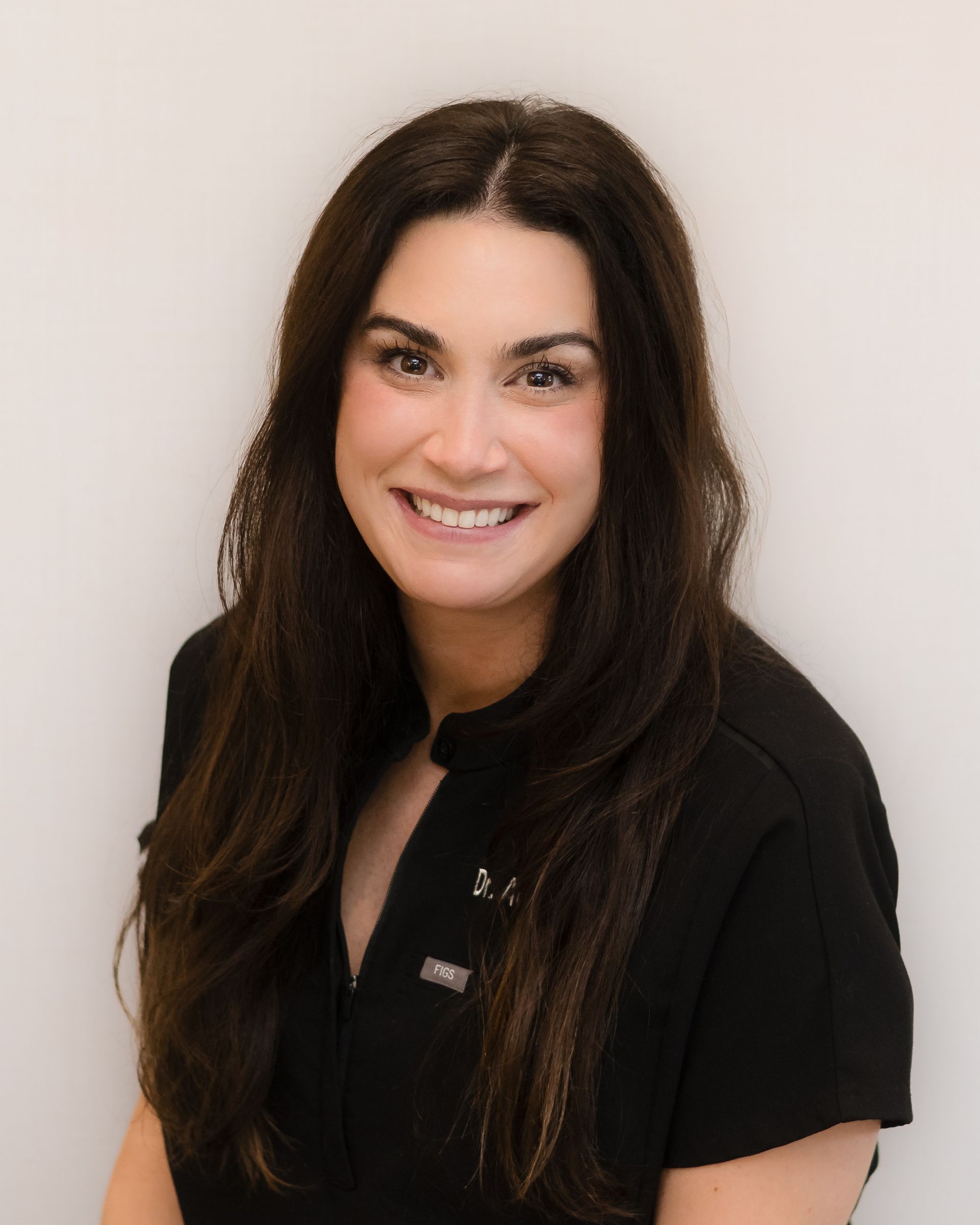 Smiling woman with long dark hair in a black top against a light background