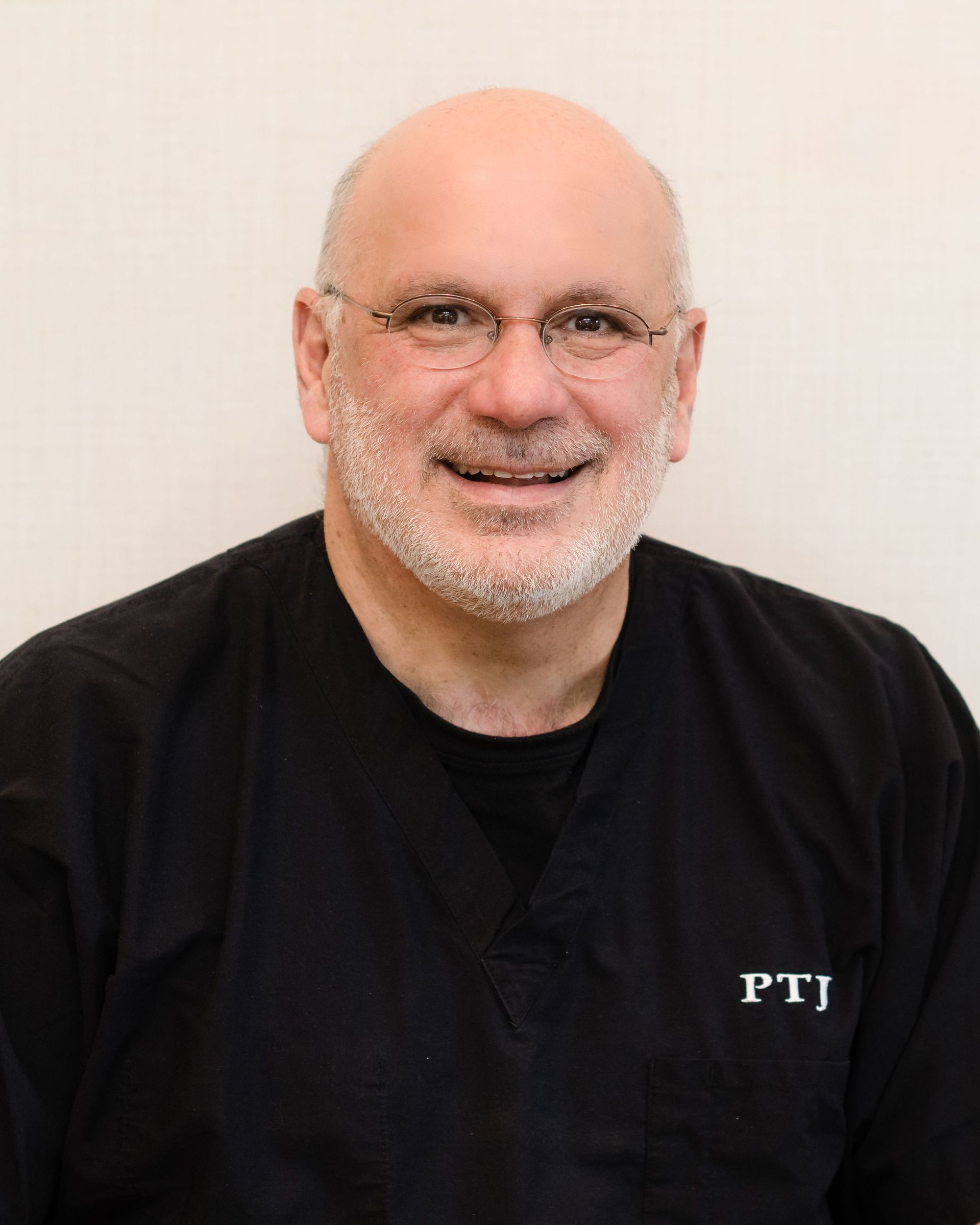Smiling bald man with glasses in a black shirt against a light background