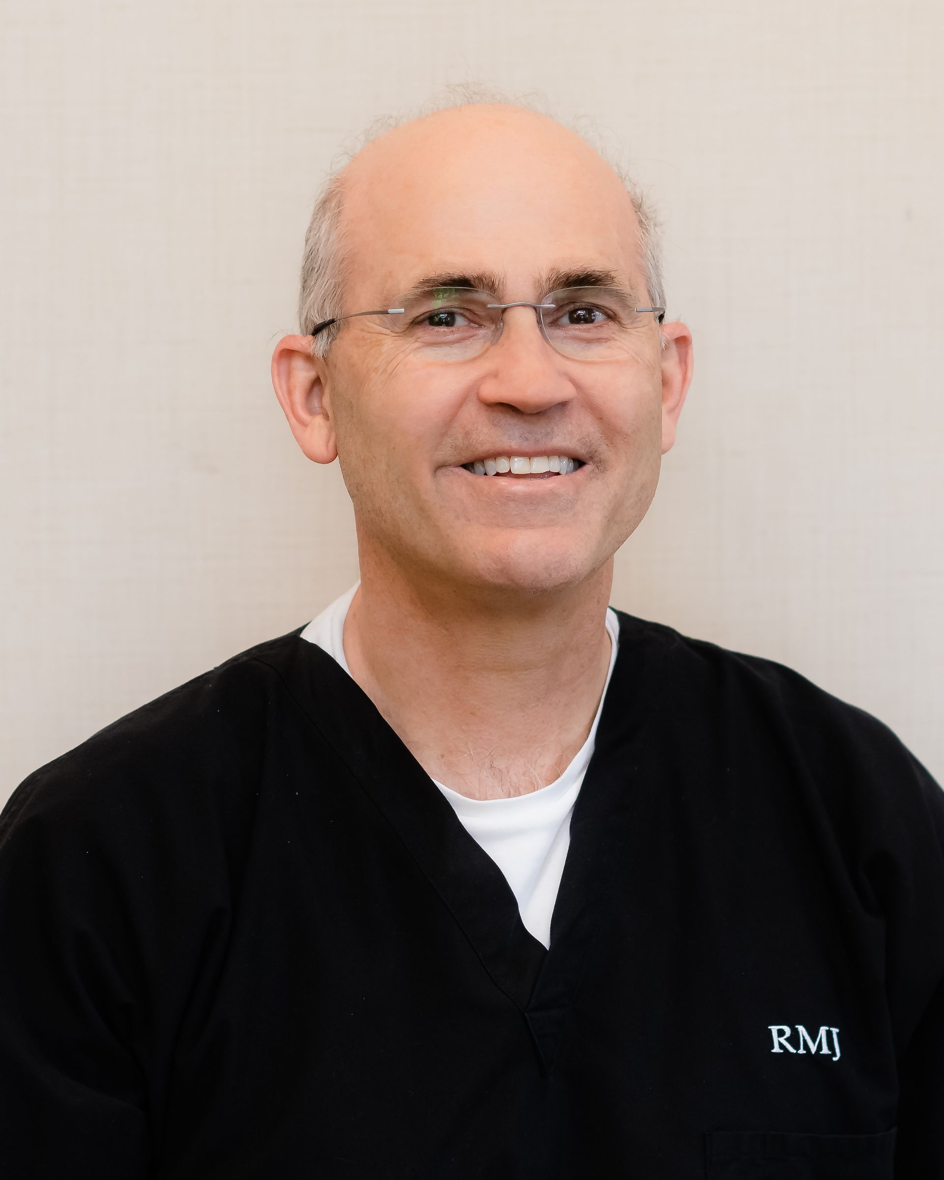 Smiling person in black scrubs with glasses against a plain light background