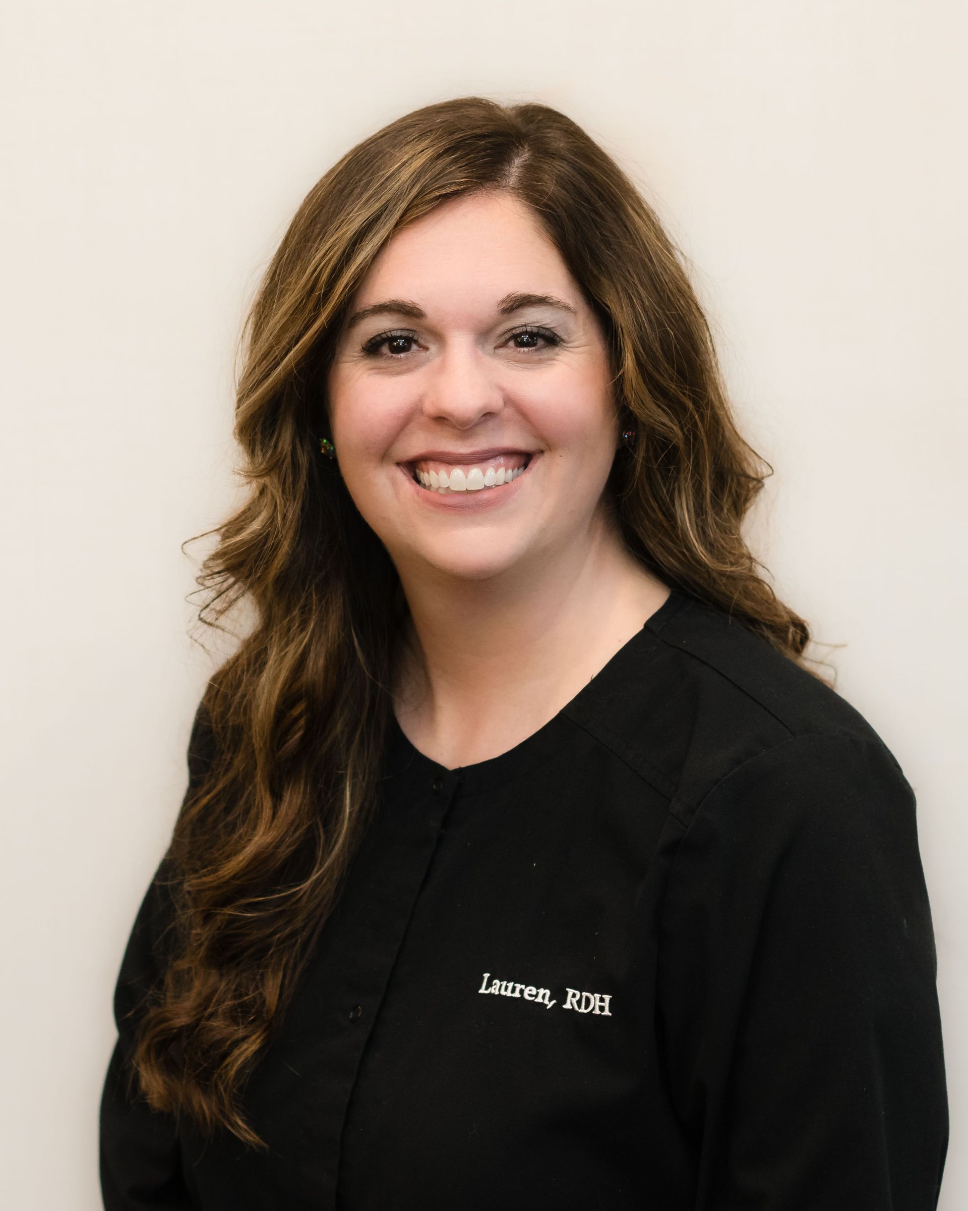 Smiling woman in a black shirt against a light background, wearing long brown hair.
