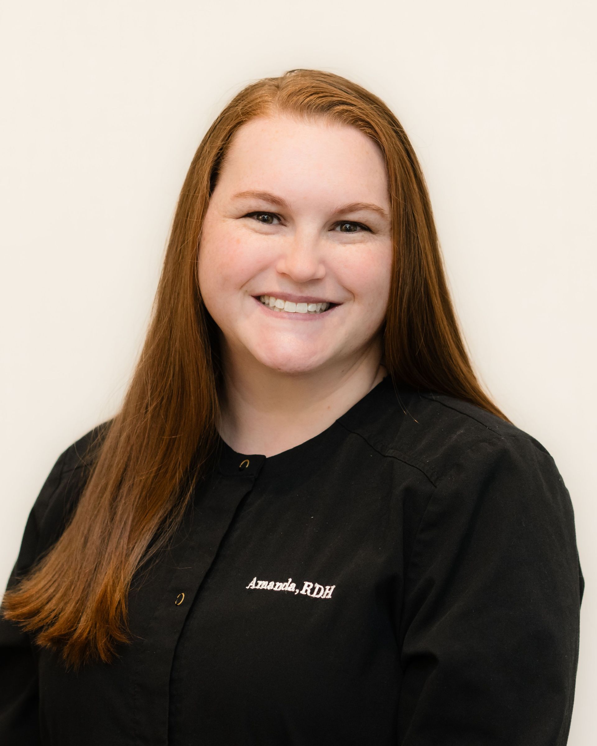 Smiling person with long red hair wearing a black shirt against a light background