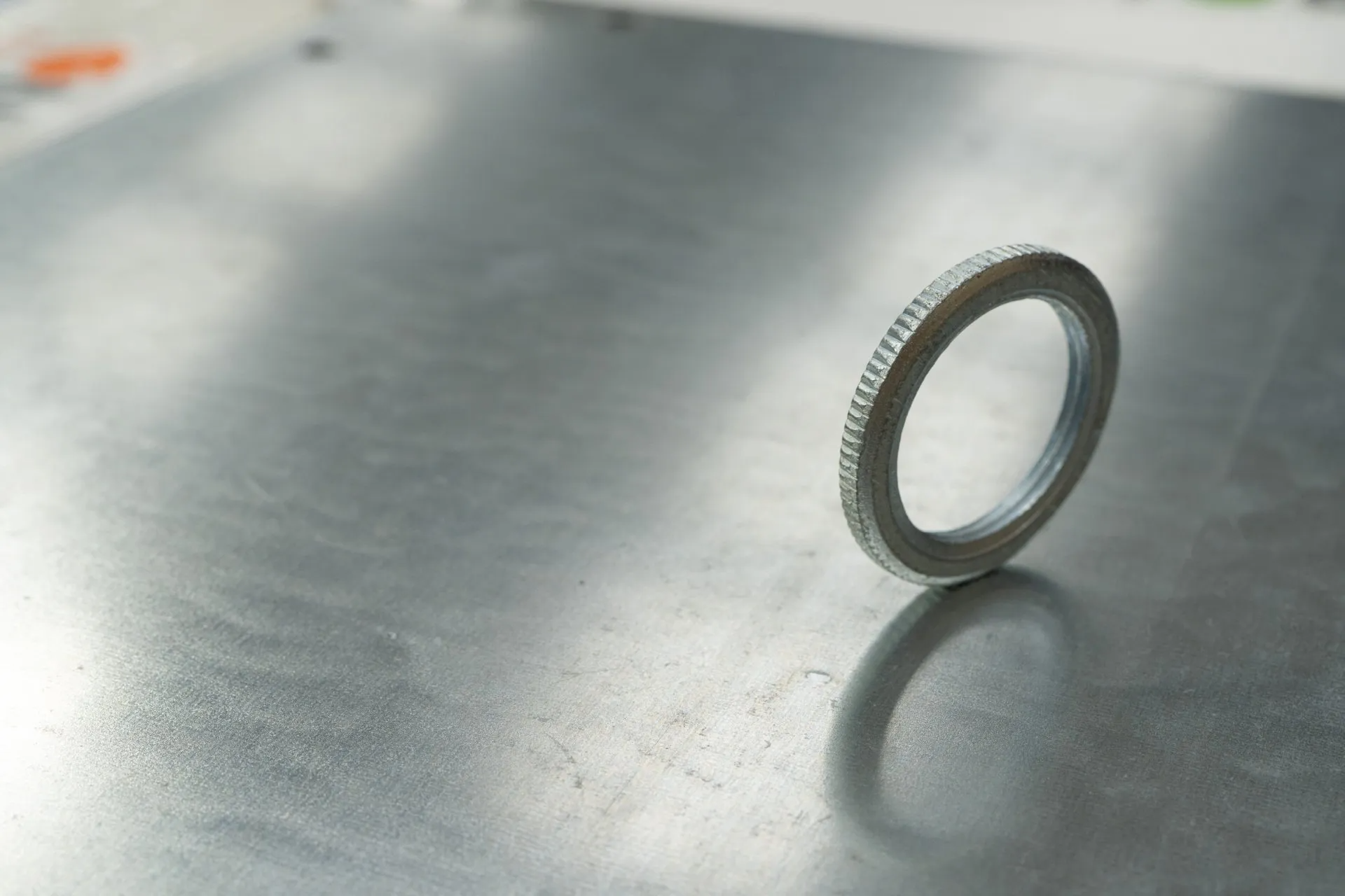 Metal washer standing on a metal surface, casting a shadow.