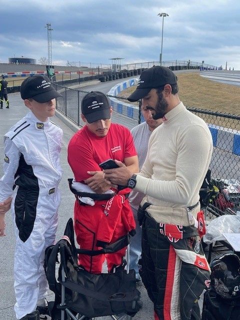 Four people looking at a phone near a racetrack.
