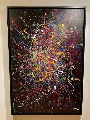 Abstract schilderij met kleurrijke spetters en lijnen tegen een donkere achtergrond, in een zwarte lijst.