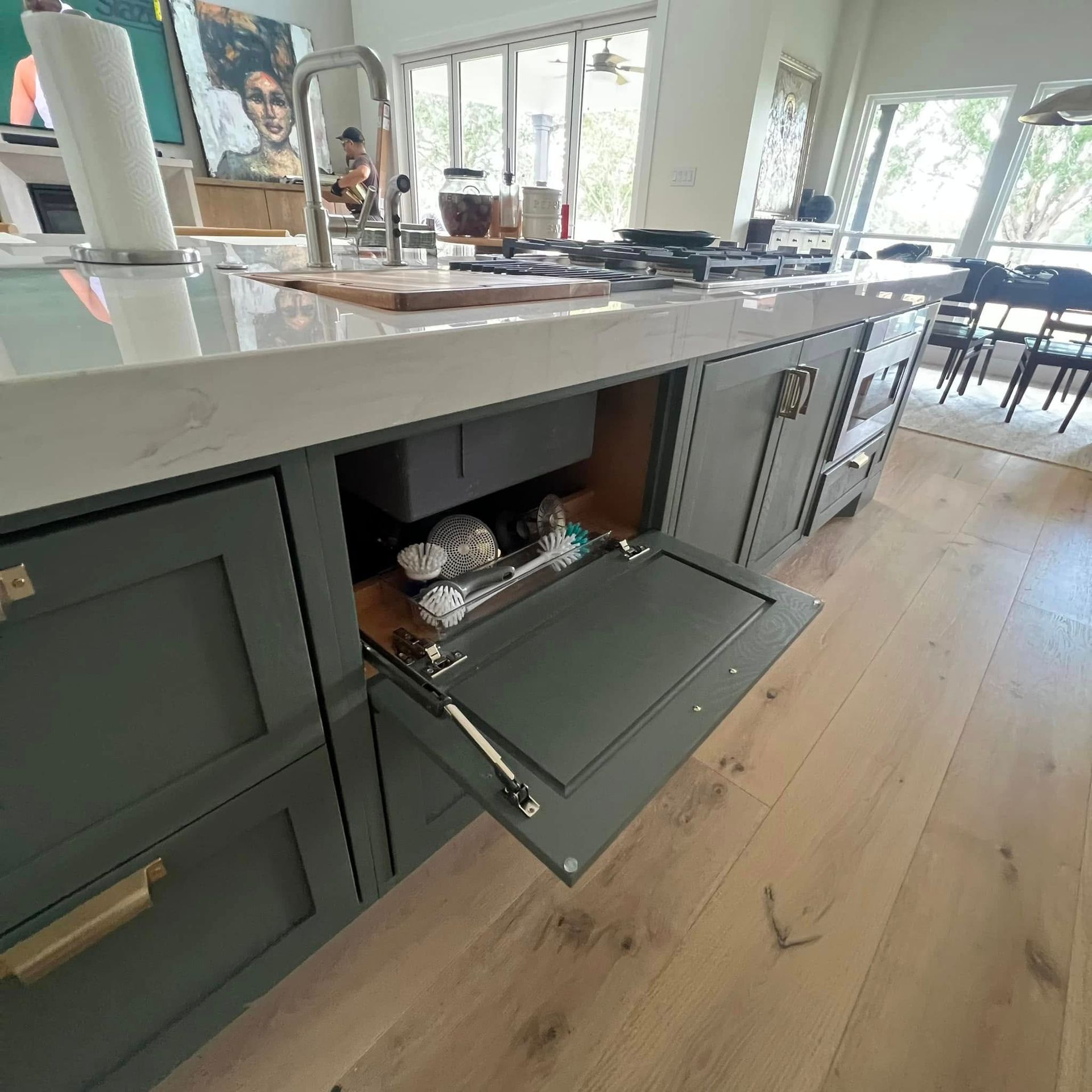 A low-angle view of a grey kitchen island showing an open tilt-out sponge tray cabinet underneath the countertop.