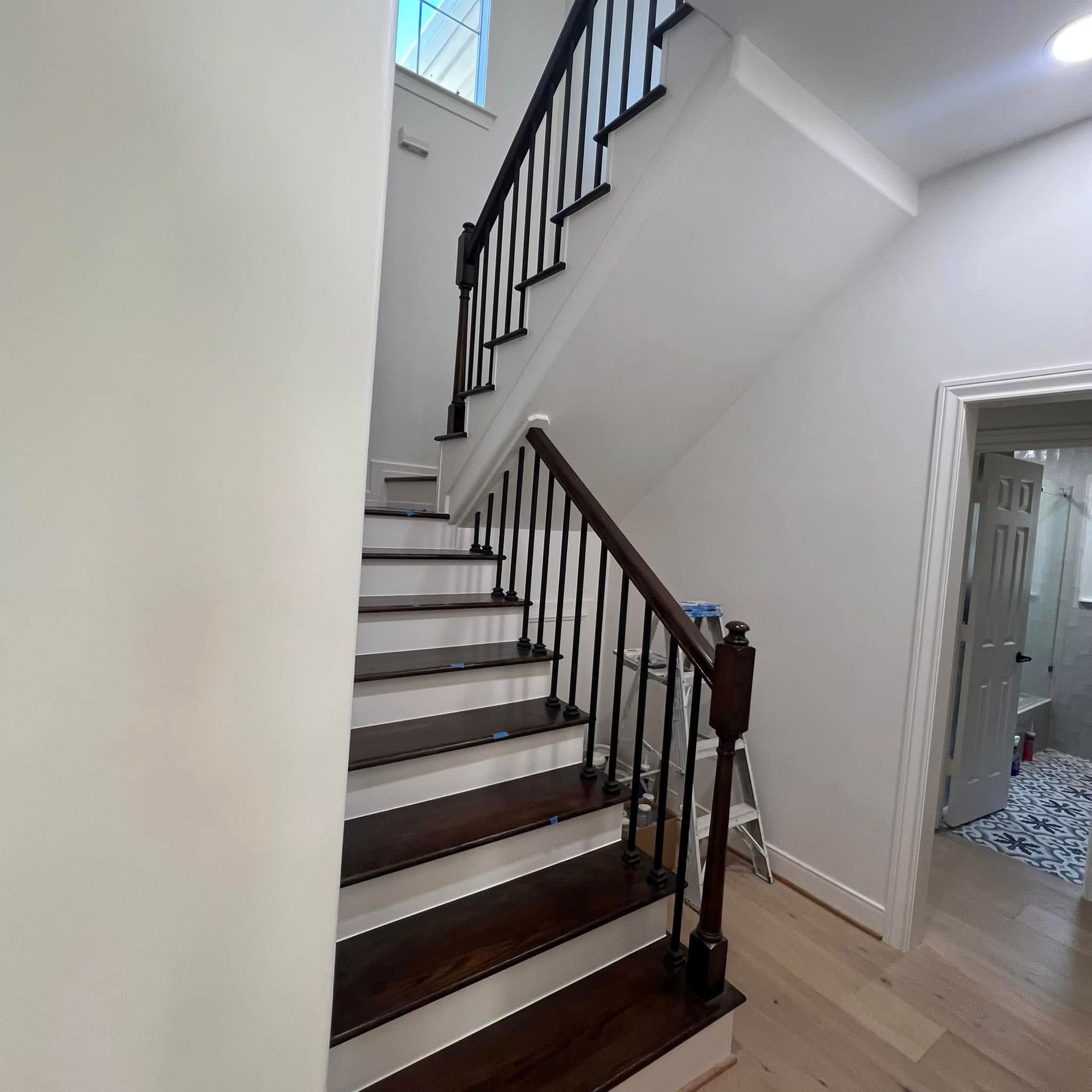 A wooden staircase with dark steps and white risers, featuring a black metal railing, leading to an upper floor.