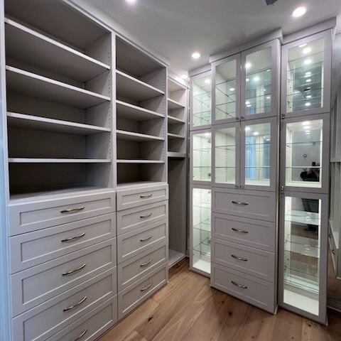 A walk-in closet with light wood cabinetry, shelving, and a doorway leading to an adjoining storage area with tiled floors.