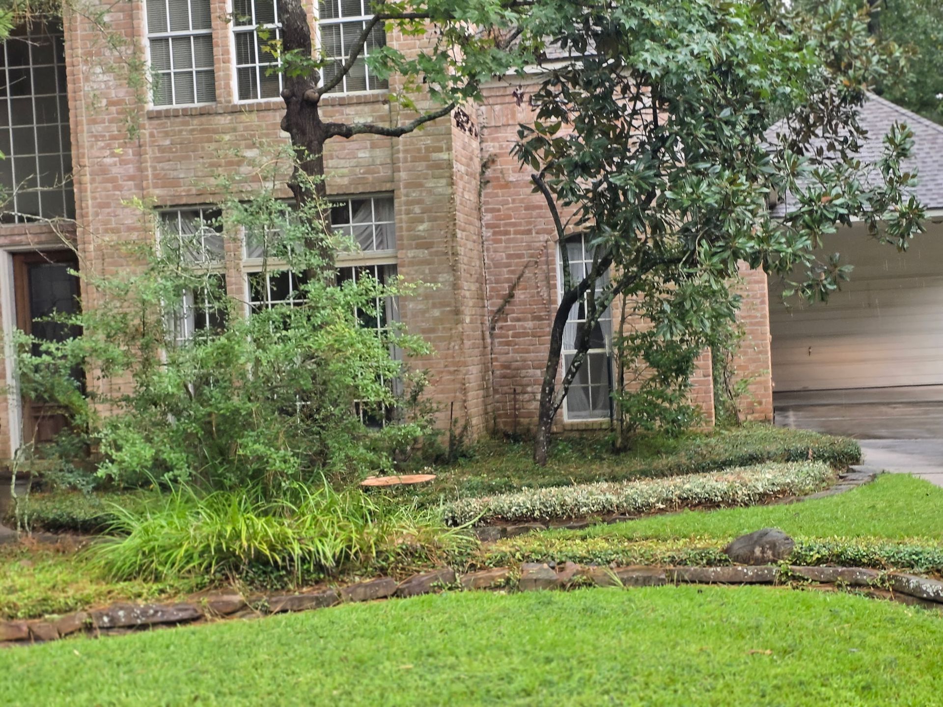 Brick house with a front garden, shrubs, and a garage driveway.