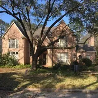 Brick two-story suburban house with large front yard and a tree shading the facade