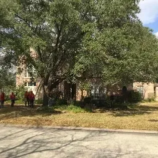 Tree-shaded courtyard with a tan building and a few people standing near the left side.
