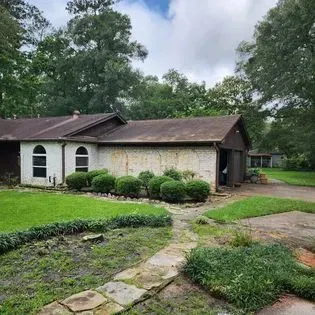 Single-story brick house with brown roof, green lawn, stone path, and trees in the yard