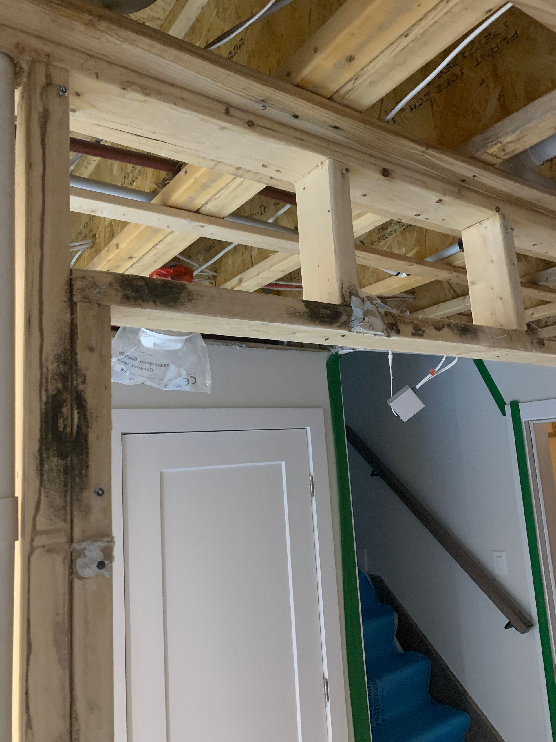 Un cadre de porte inachevé en construction à l'intérieur d'un bâtiment, laissant apparaître les montants en bois et les solives de plafond.