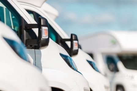 A row of white vans are parked next to each other in a parking lot.
