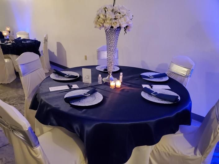 Round banquet table set with black tablecloth, white plates, candles, and floral centerpiece in a softly lit room