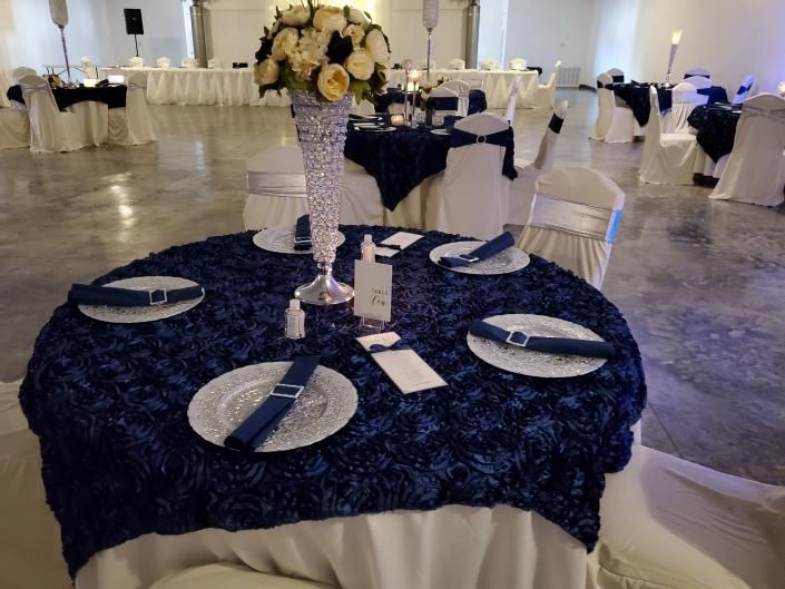 Round navy table with white plates, silverware, and a tall floral centerpiece in a banquet hall