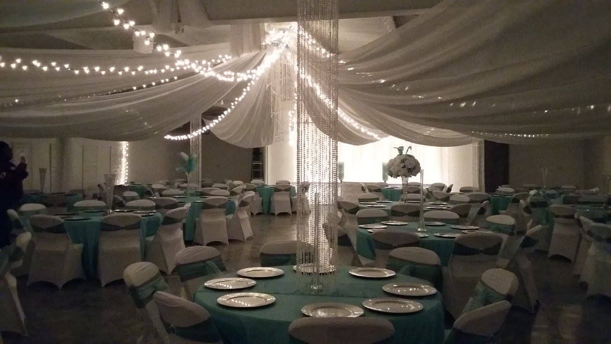 Decorated banquet hall with teal table settings and draped ceiling lights, ready for an event