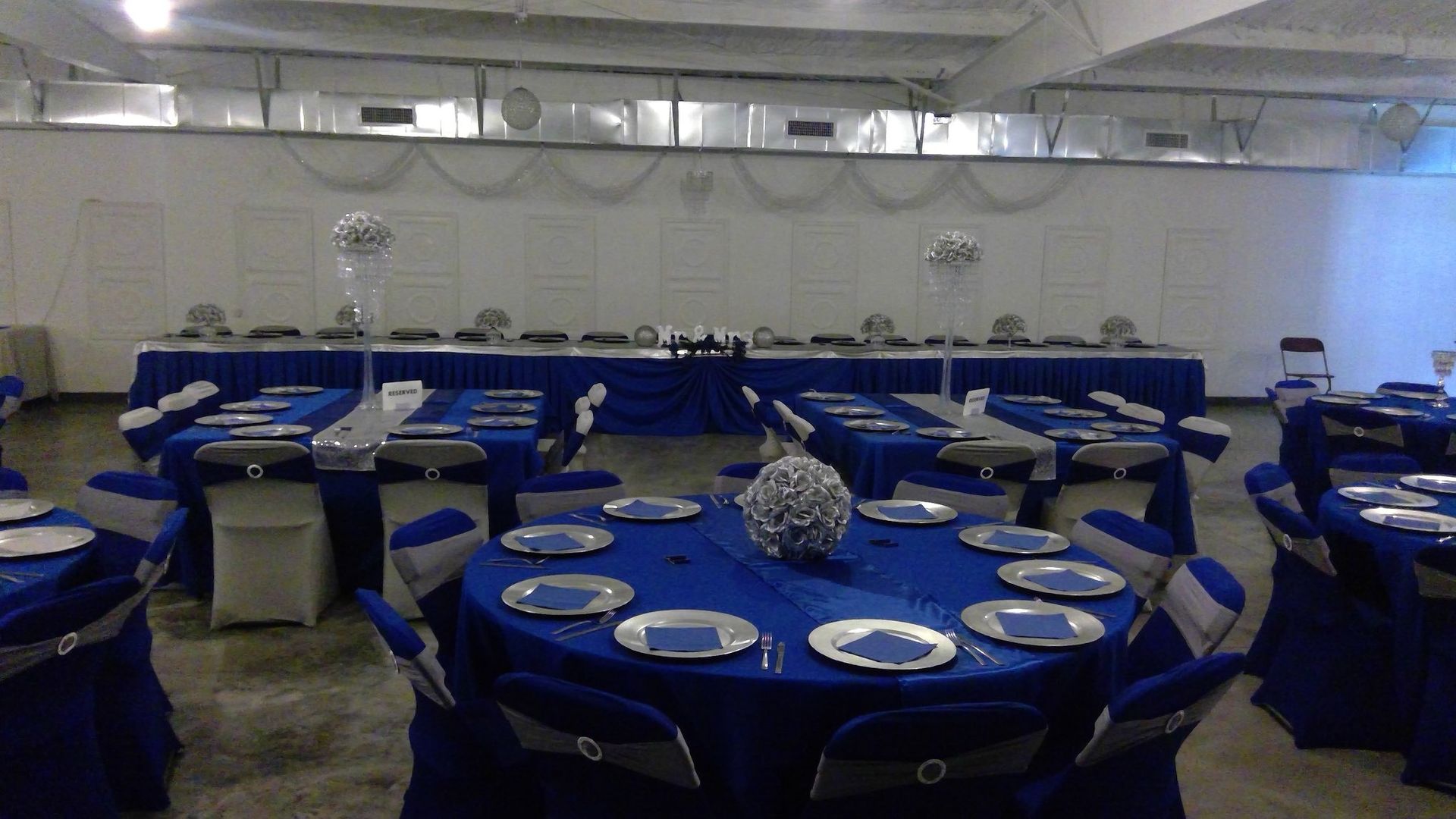Banquet hall with blue-covered round tables, set with white plates and chairs around a long head table