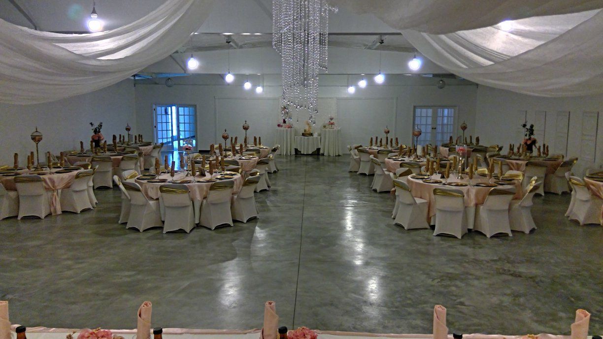 Large banquet hall set for an event, with round tables, beige chairs, white draped ceiling, and chandeliers.