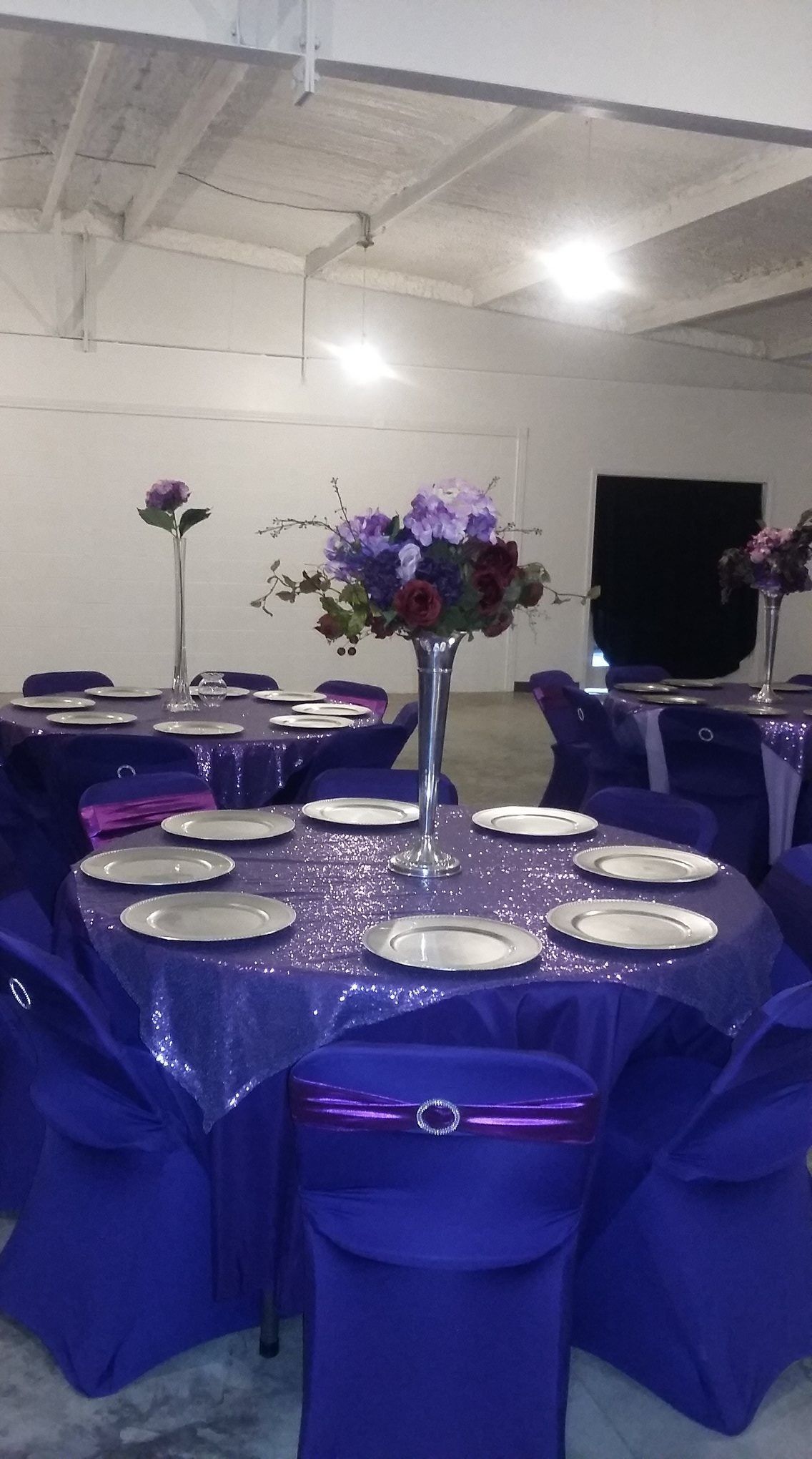 Purple-decorated banquet table with white plates and a floral centerpiece in a banquet hall