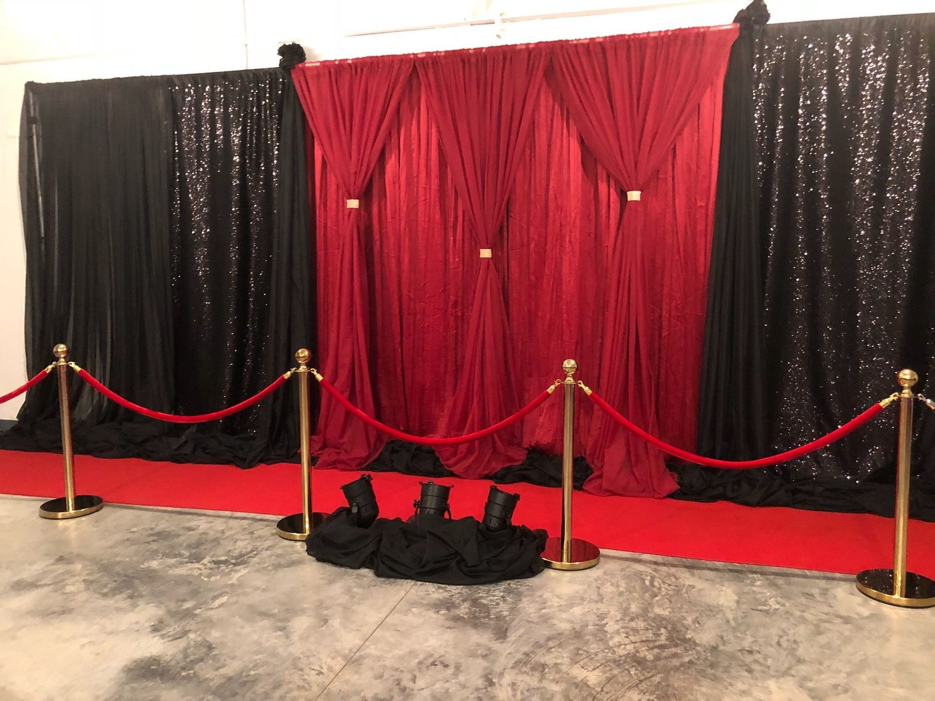Red and black draped photo backdrop with velvet ropes and gold stanchions on a red carpet.