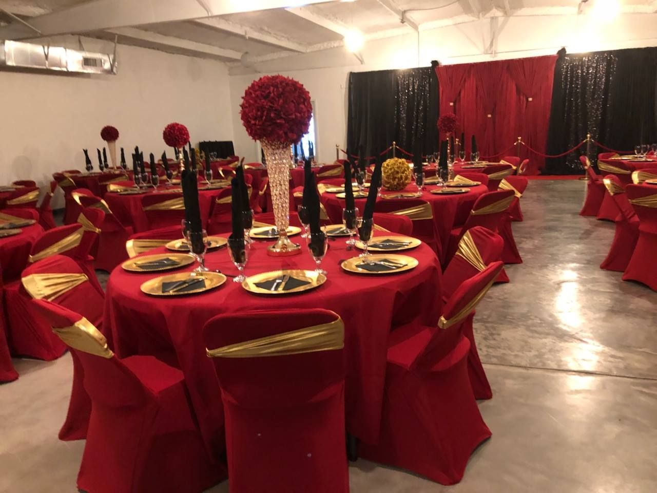 Red-and-gold banquet tables set in a decorated event hall with black and red drapes.