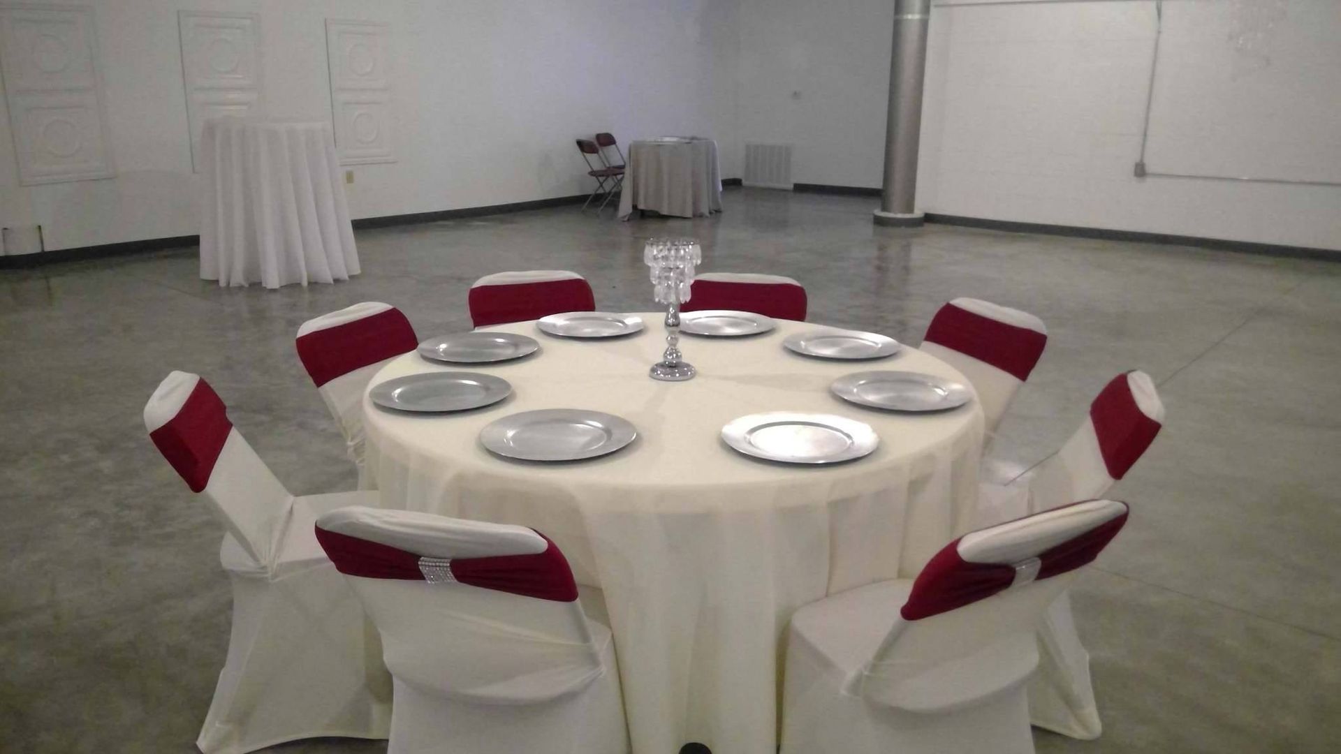 Round banquet table with white cloth and red chair covers in a plain hall