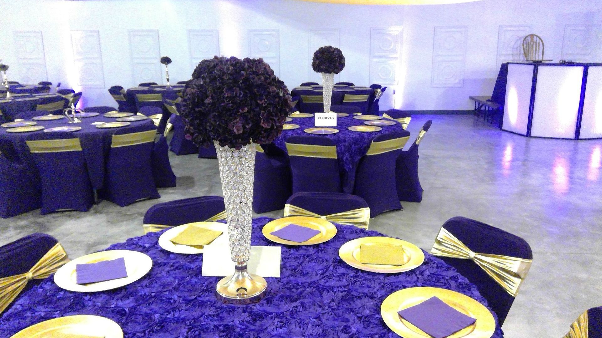 Banquet hall with round tables set in purple and gold, centered by a tall floral centerpiece