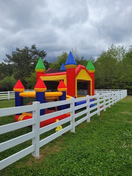 Colorful inflatable bounce house behind a white fence on a grassy field under cloudy skies