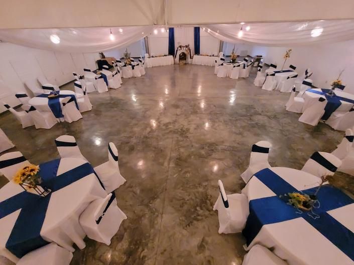 Banquet hall set with round tables, white chair covers, and blue table runners on a polished floor