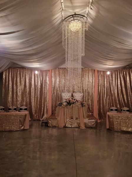 Elegant event tent with rose-gold drapes, chandeliers, and decorated tables around a central floral display