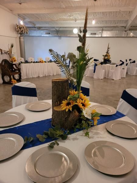Round banquet table with blue runner, white plates, and sunflower centerpiece in a decorated event hall