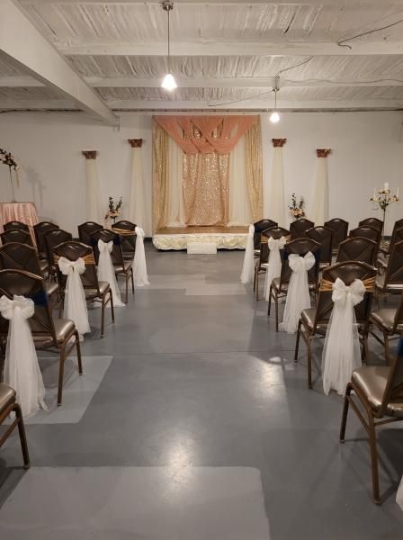 Rows of white chairs facing a decorated stage in a banquet hall with cream and peach drapes