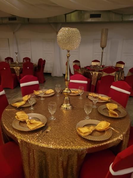Gold-sequined banquet table with red chairs and gold place settings in a white event tent