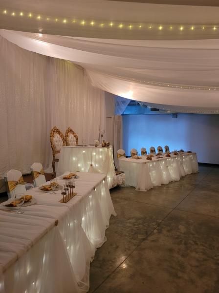 Decorated banquet hall with white-draped tables, string lights, and a blue-lit backdrop