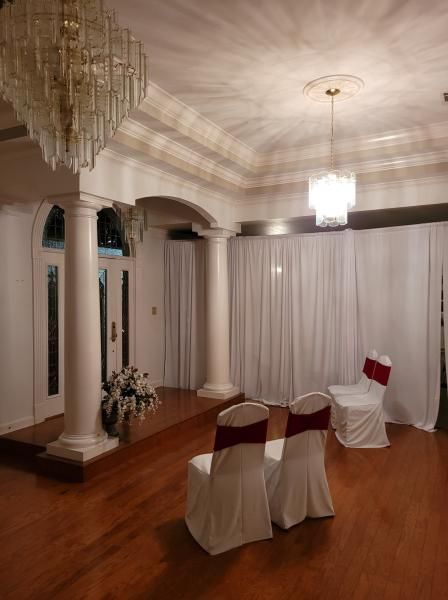 Elegant reception room with chandeliers, white drapes, and chair-covered seating on a polished wooden floor