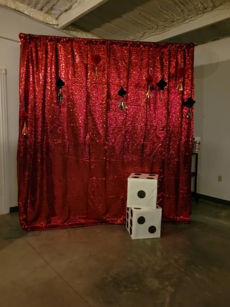 Red shimmering curtain backdrop with two white dice-shaped boxes on the floor in an indoor room.