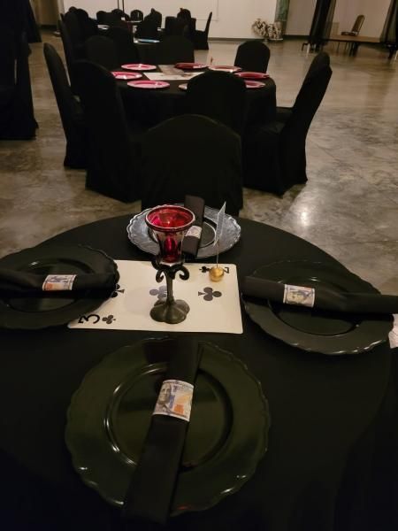 Black table set with red centerpiece in a banquet hall, with more decorated tables in the background