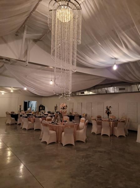 Elegant banquet hall with draped white ceiling, chandeliers, and round tables set for an event