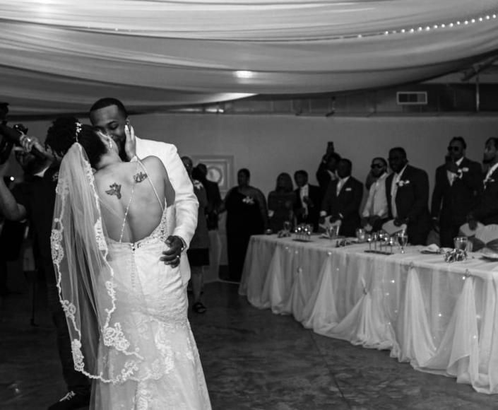 Bride and groom kissing at a wedding reception, with guests and banquet tables in the background.